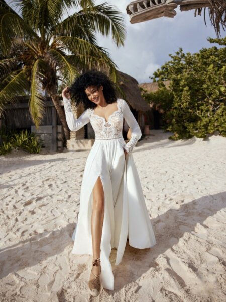 Herve Paris Becca A line wedding dress with lace bodice and long sleeves front walking on beach.