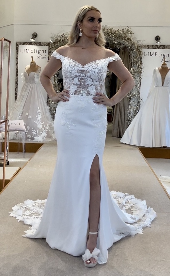 Limelight Loves private label fitted wedding dress with plain crepe skirt, leg split, lace fitted bodice with off the shoulder neckline and stunning lace train. Front view sleeves removed..