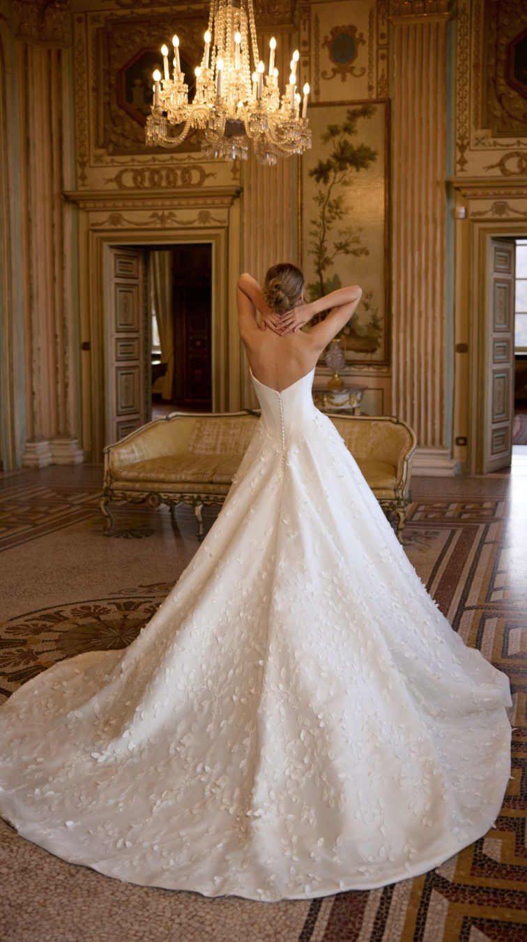 Randy Fenoli Ivy wedding dress with plain basque bodice optional drop drape sleeves and trailing leafy lace over an A-line skirt strapless back view.