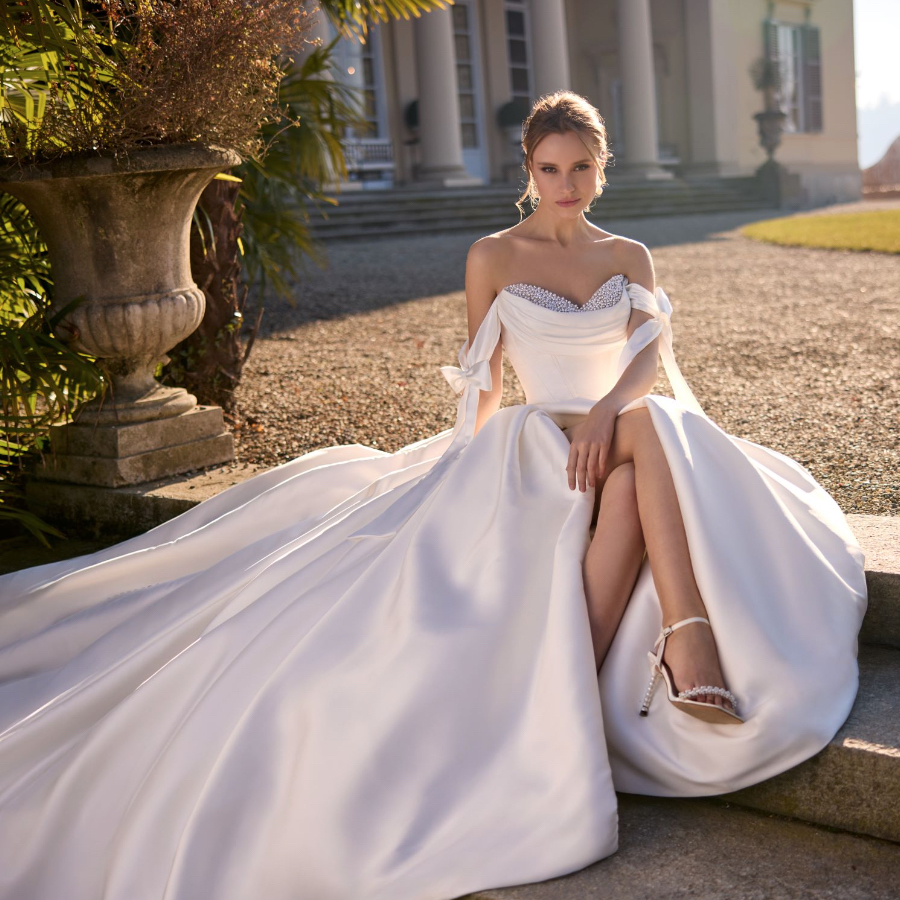 Randy Fenoli Jaqueline ballgown with basque bodice and cowel neckline available with or without beading and drop drape straps front view sitting.