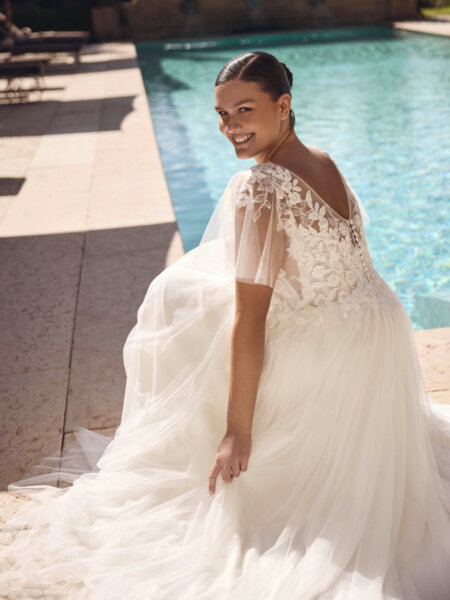 Modeca Curves Jada plus size wedding dress with plain a-line tulle skirt V neck lace bodice and detachable flutter sleeves back sitting view.
